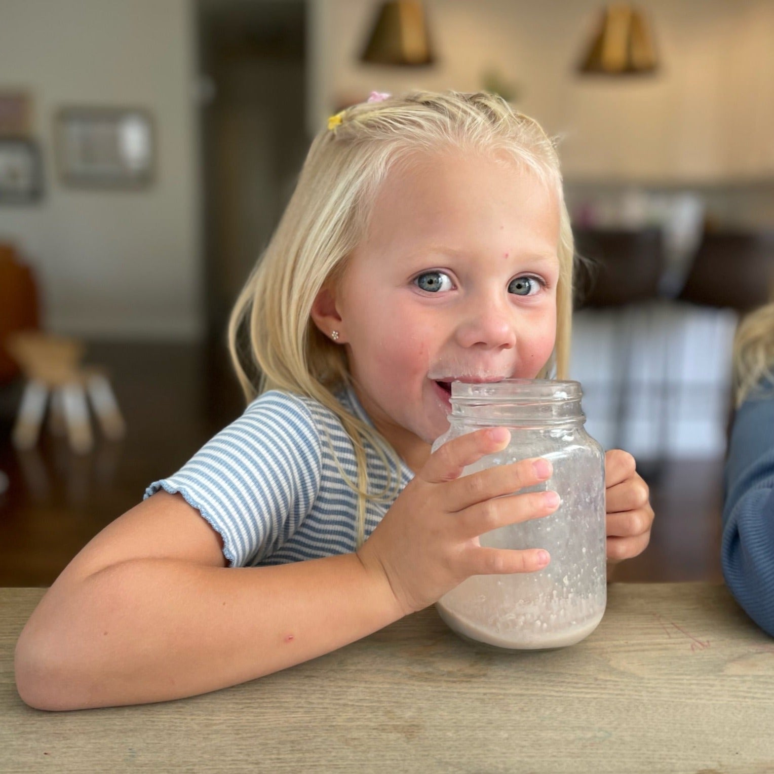 smiling young child sitting at kitchen counter holding glass of chocolate mighty milk up to mouth with a milk moustache