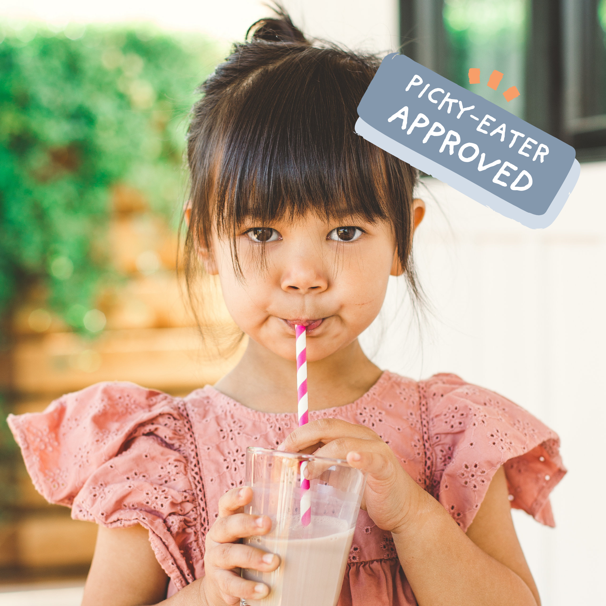 Child drinking a glass of Mighty Milk from a Straw with a Picky-Eater Approved icon in top corner